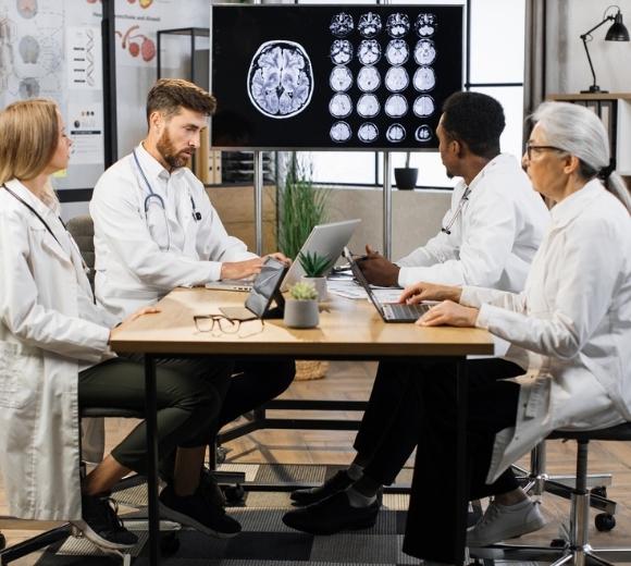 Several neurohospitalists meeting with laptops on table looking at a brainscan